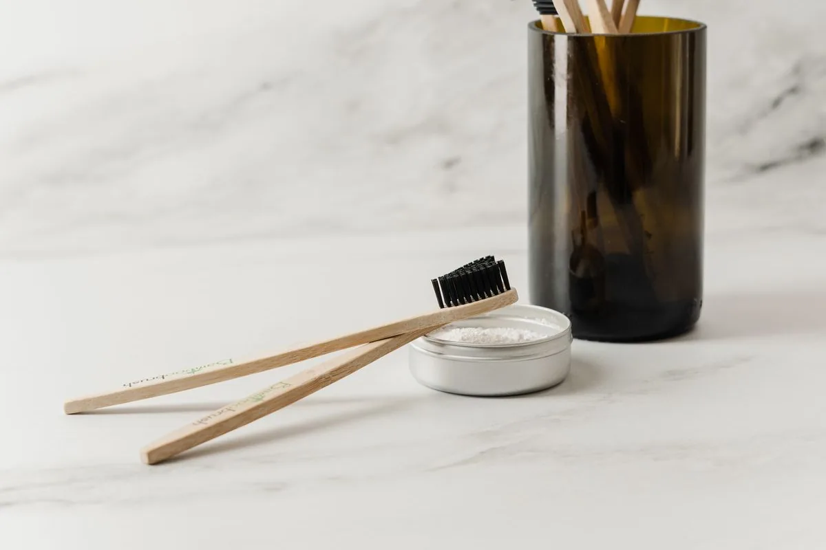 Toothbrushes in a glass cup and a brush resting on a bathroom counter