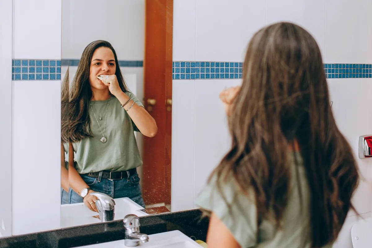 Woman brushing her teeth in front of a bathroom mirror as part of a daily oral hygiene routine