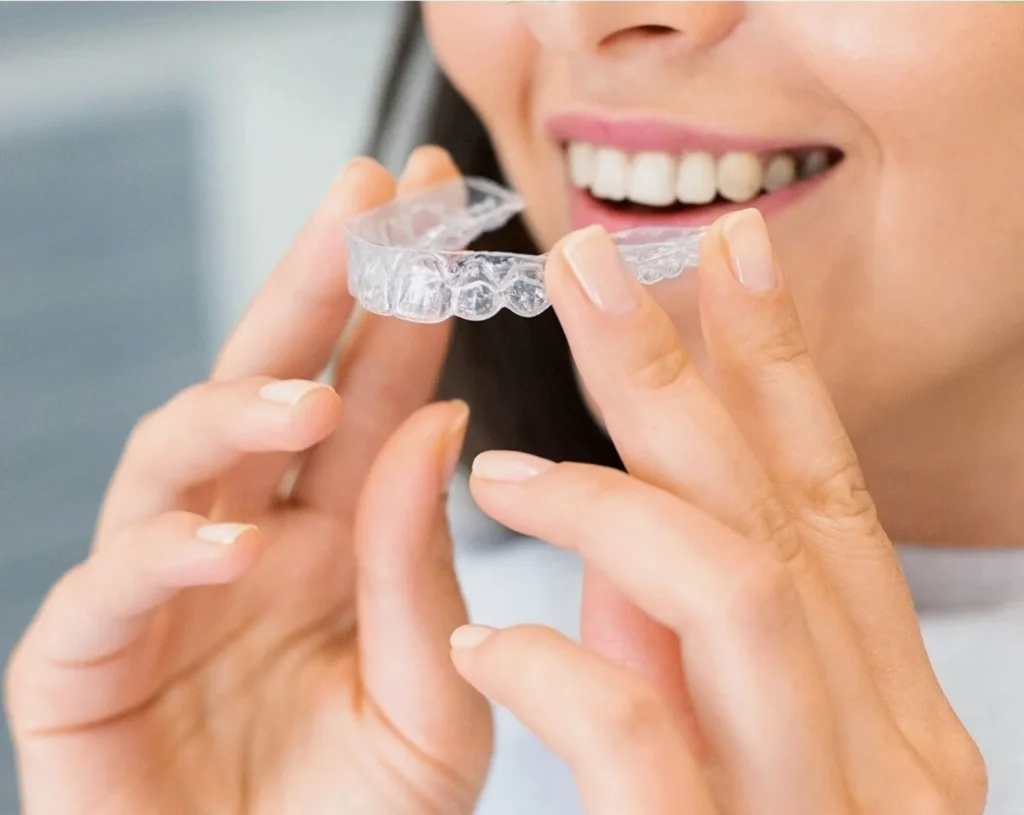 A smiling woman putting in a clear aligner